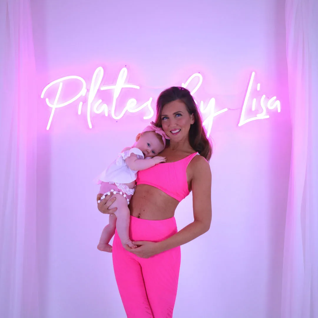 Lisa joyfully demonstrates a Pilates exercise, wearing pink and purple activewear, emphasizing core and waist strength.